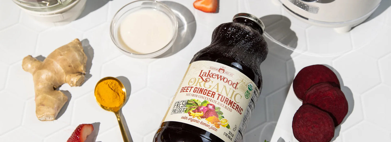 Bottle of Lakewood Organic Sweet Ginger Turmeric on a white surface with ingredients like ginger root and turmeric.